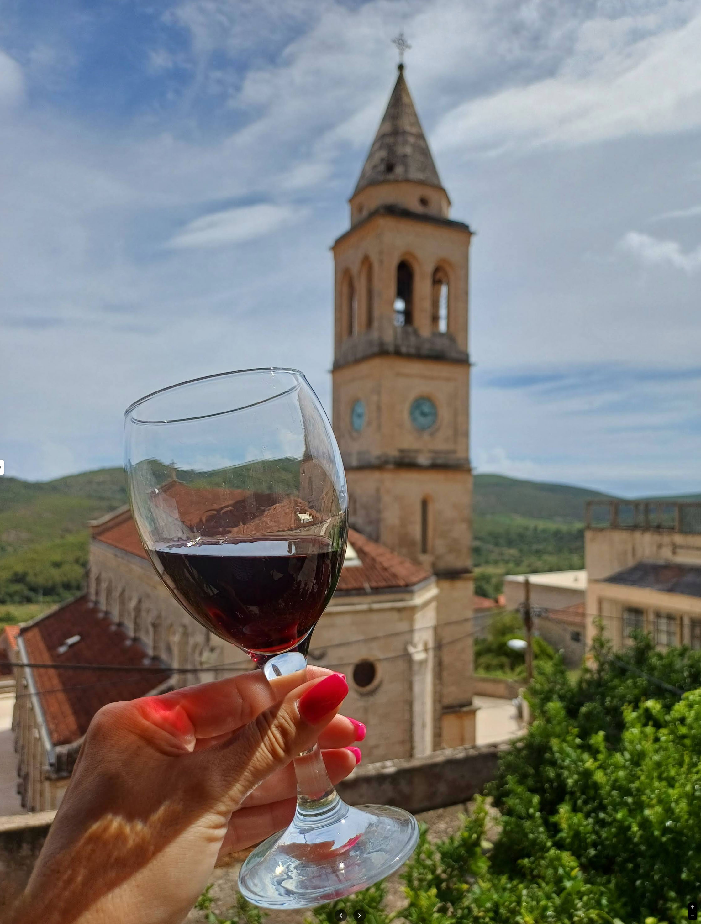 A glass of Barbazza red raised against the Smokvica bell-tower, terracotta roofs and green hills behind