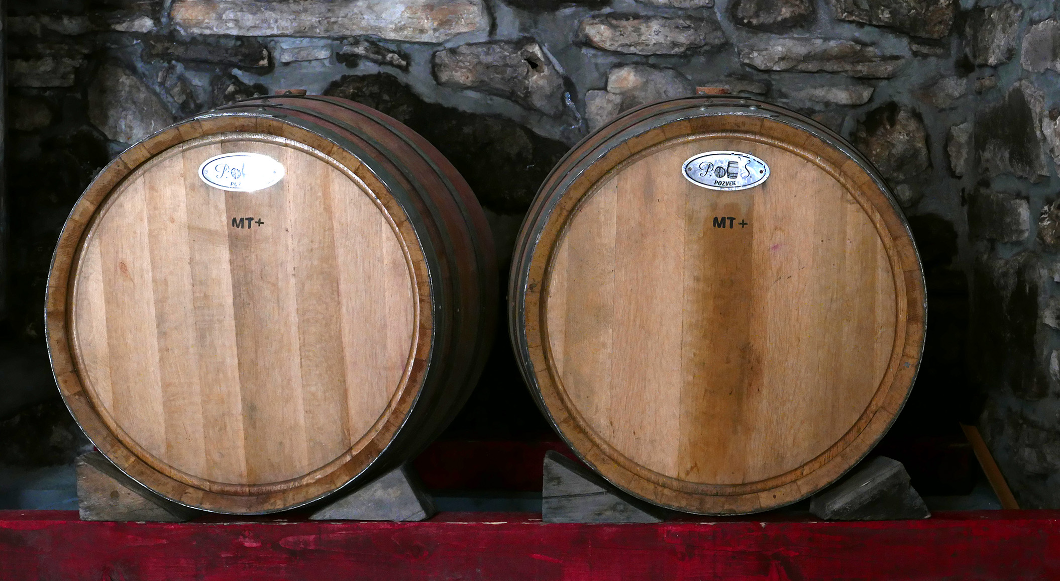 Two oak barrels marked MT against the cellar's bare stone wall