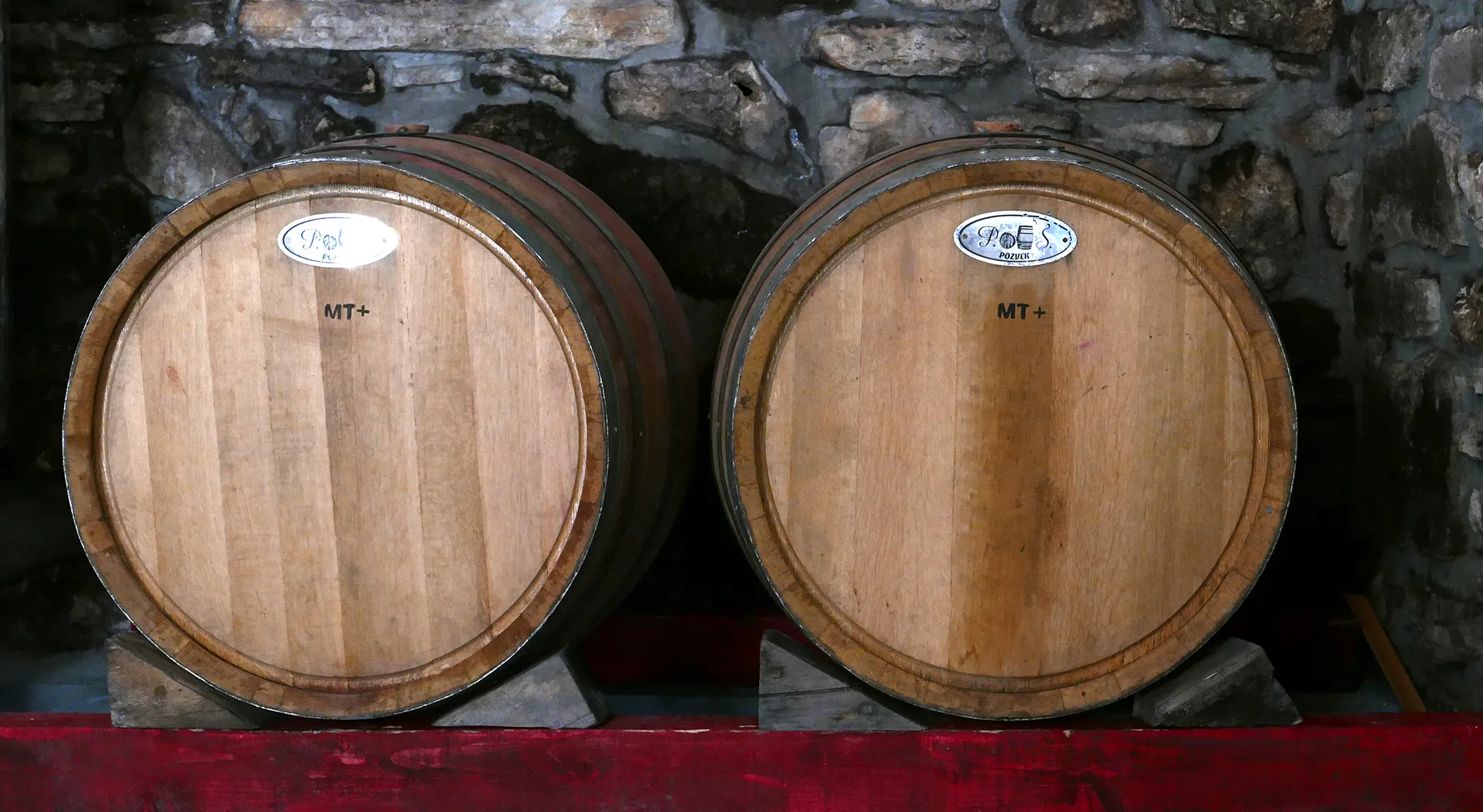 Two oak barrels marked MT against the cellar's bare stone wall