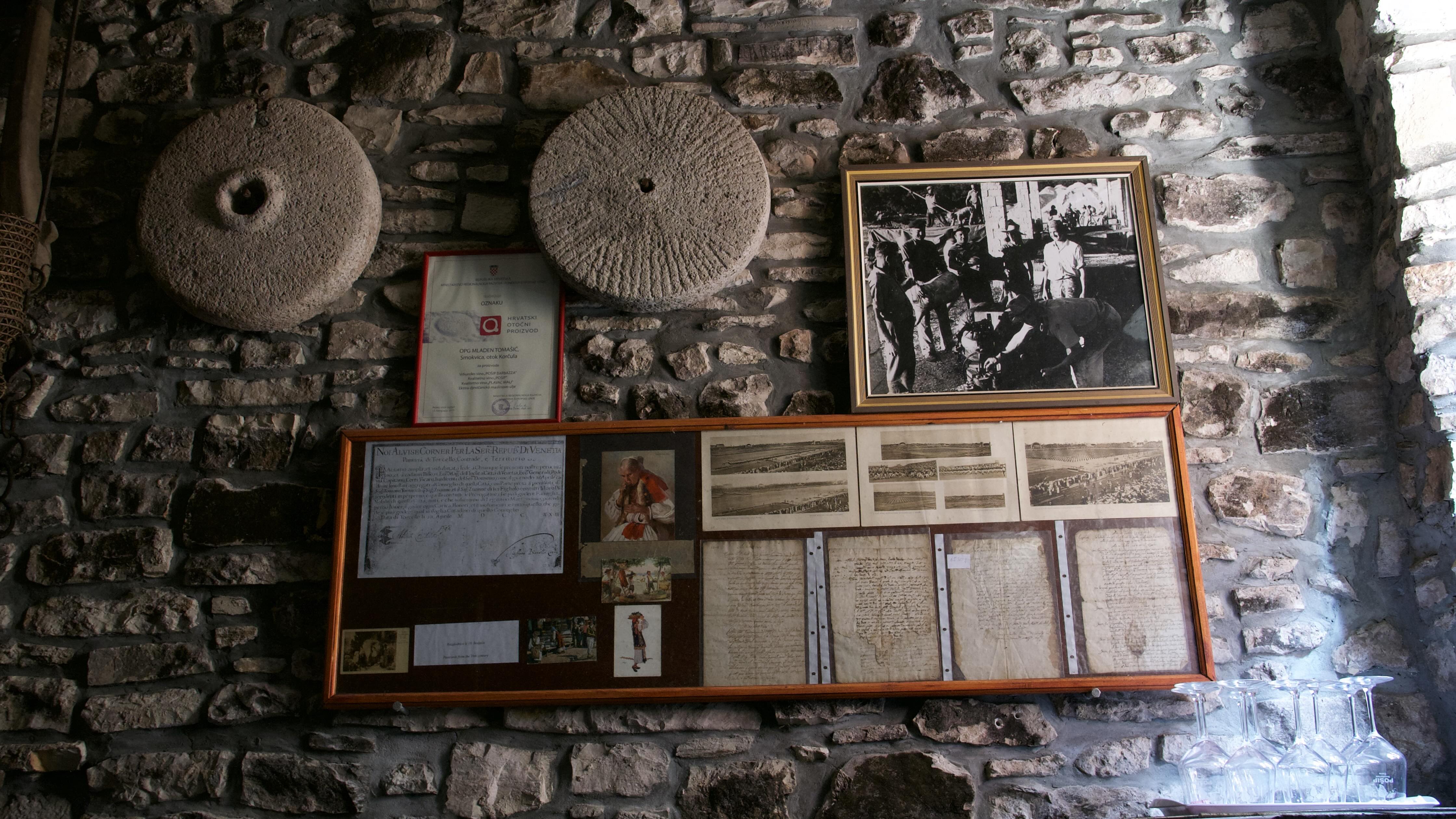 Right wall of the cellar — two ancient olive-mill stones above a black-and-white photograph and a certificate