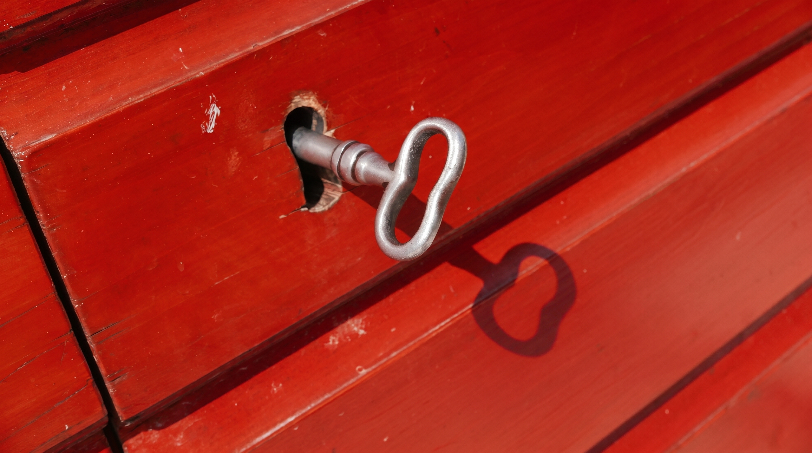 The iron key turned in the lock of the red cellar door, in full sun — its figure-eight bow casting its own shadow on the wood