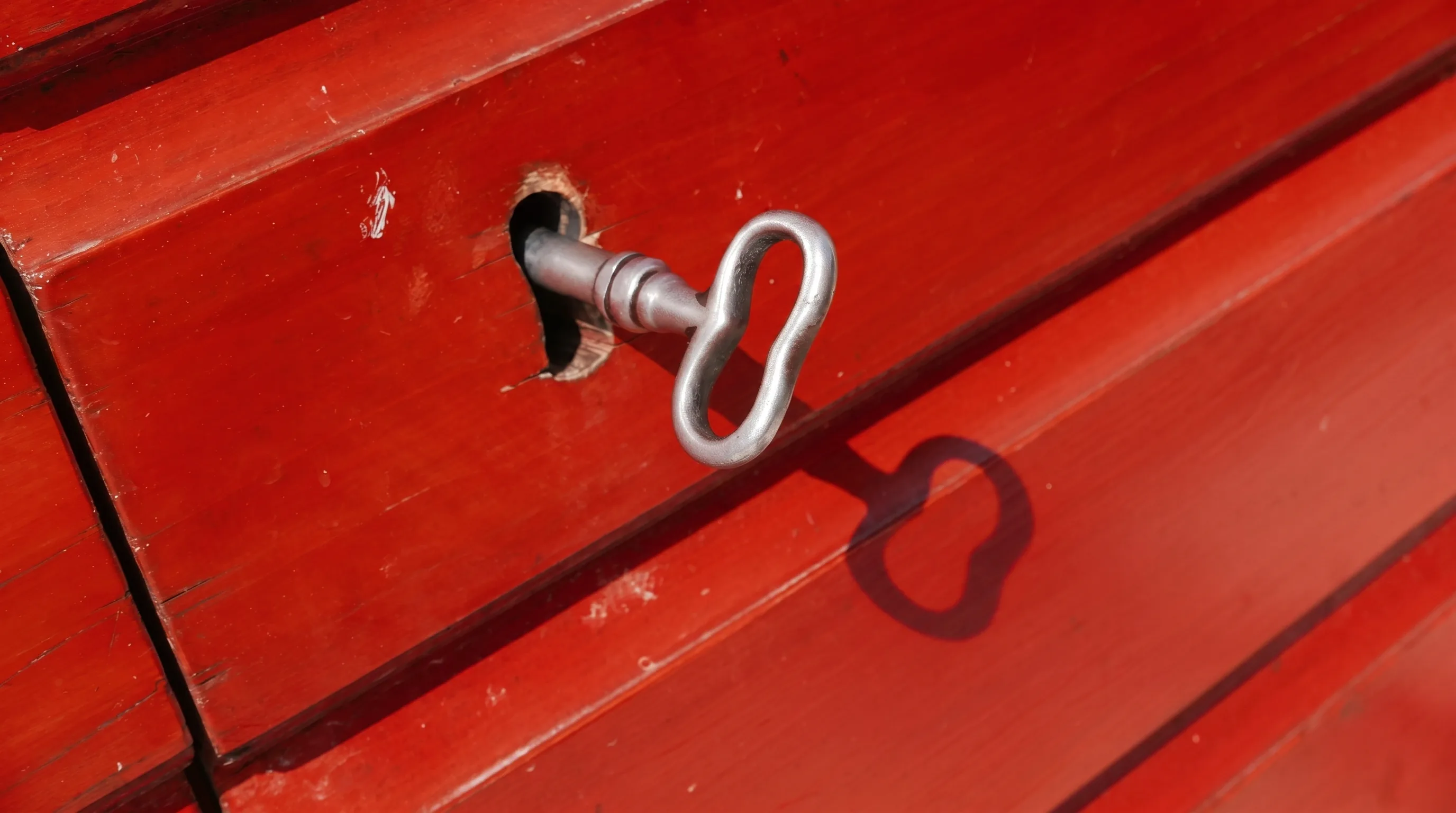 The iron key turned in the lock of the red cellar door, in full sun — its figure-eight bow casting its own shadow on the wood
